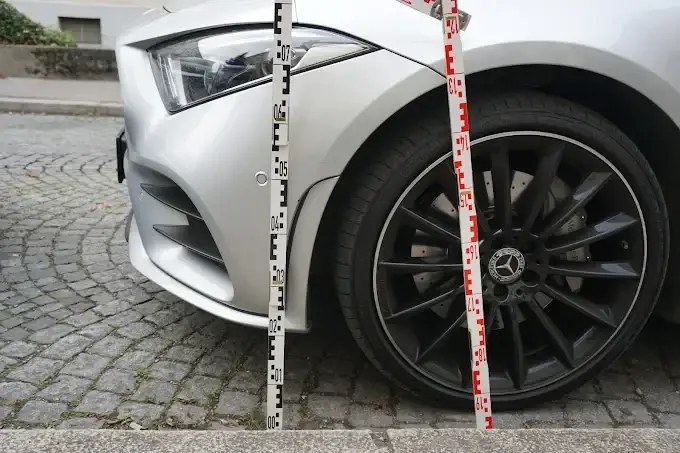 Messlatte am Vorderrad eines silbernen Mercedes zur Dokumentation von Fahrzeughöhe und Radstellung