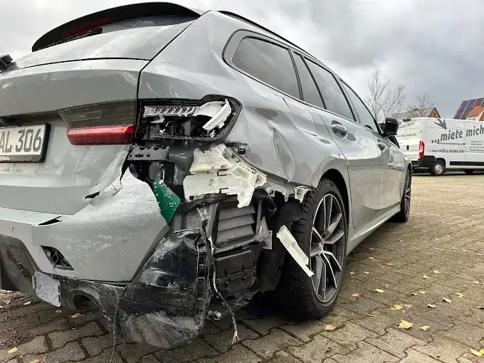 Silberner BMW 3er Touring mit abgerissenem hinterem Stoßfänger und freiliegender Trägerstruktur nach einem Heckaufprall